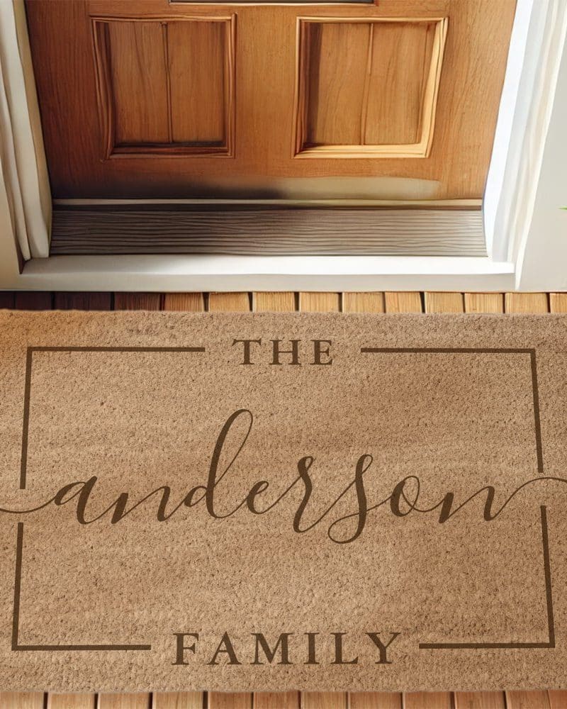Tan doormat with the words The Anderson Family in a script font within a brown rectangular frame.