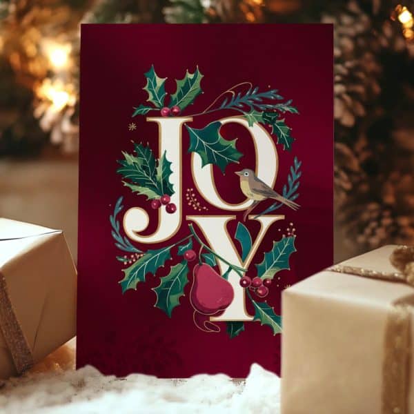 A Burgundy Christmas Card With The Word Joy In Elegant Lettering Surrounded By Holly, Berries, And A Small Bird.