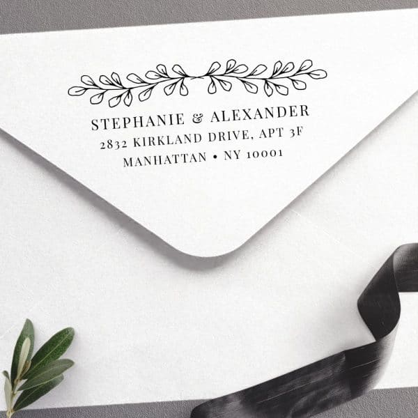 White Envelope With A Return Address Stamp Featuring Stephanie &Amp; Alexander'S Name And Manhattan Address, Accented With A Simple Leafy Design.