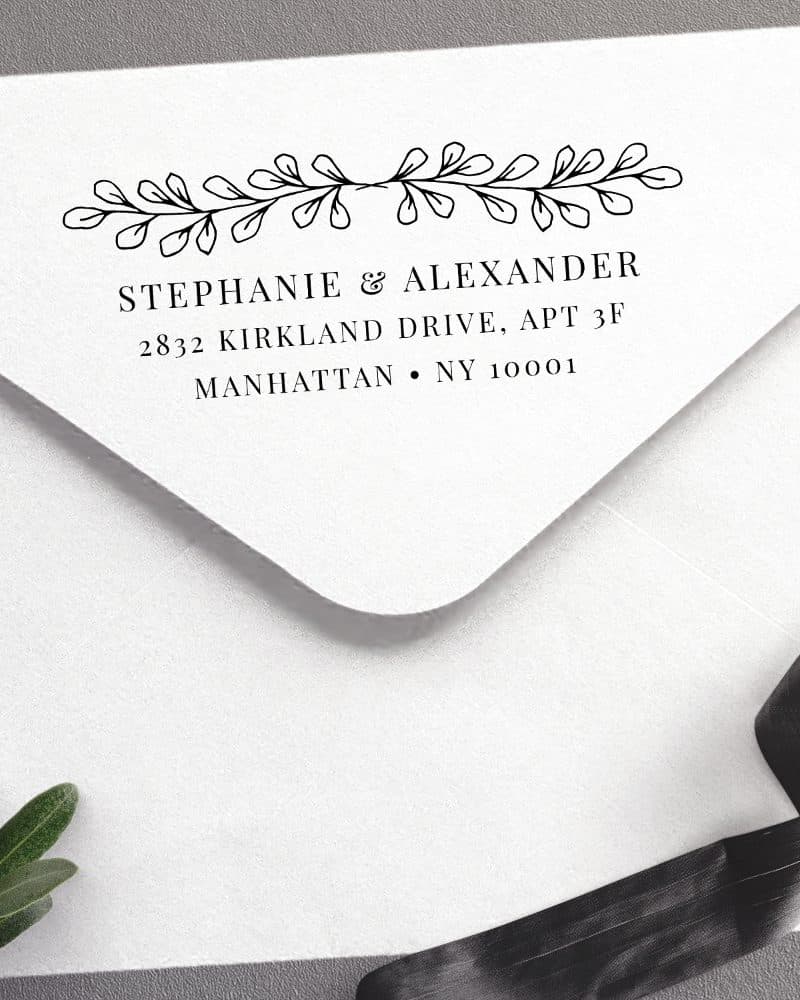 White envelope with a return address stamp featuring Stephanie & Alexander's name and Manhattan address, accented with a simple leafy design.