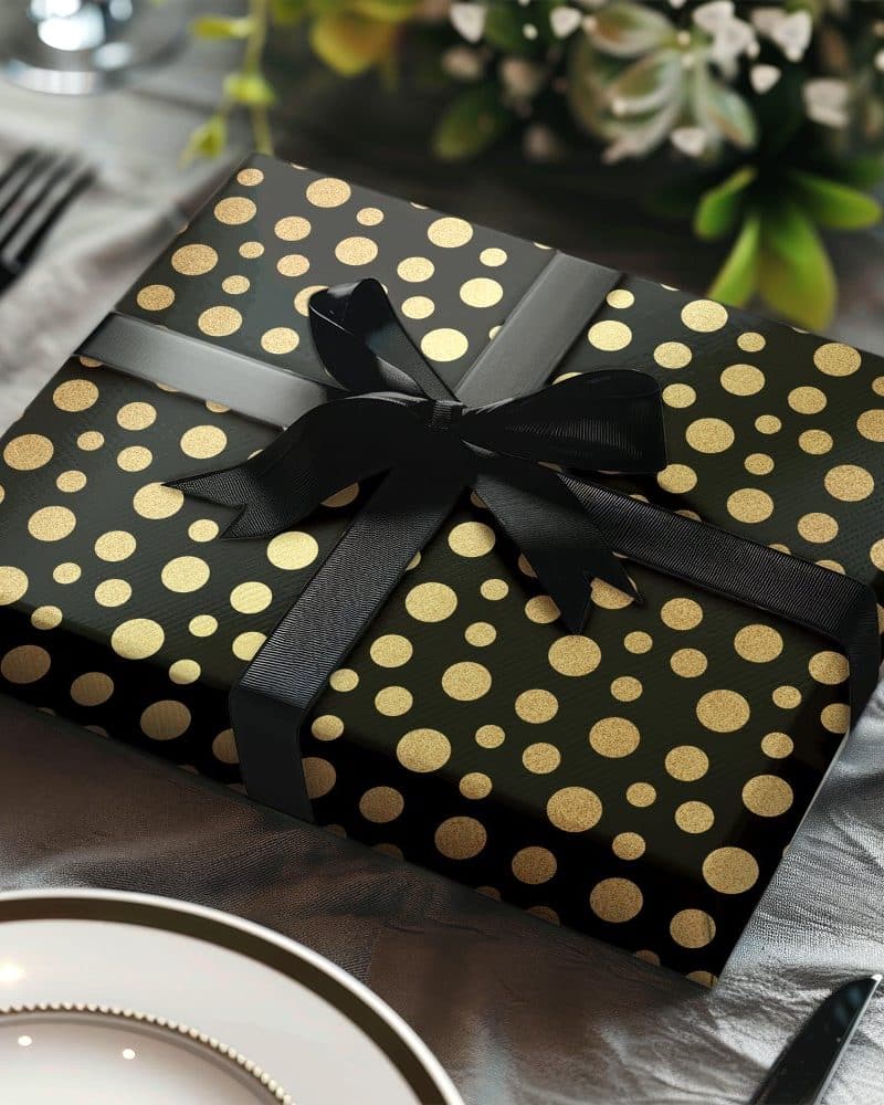 A gift wrapped in black paper with gold polka dots and a black ribbon.