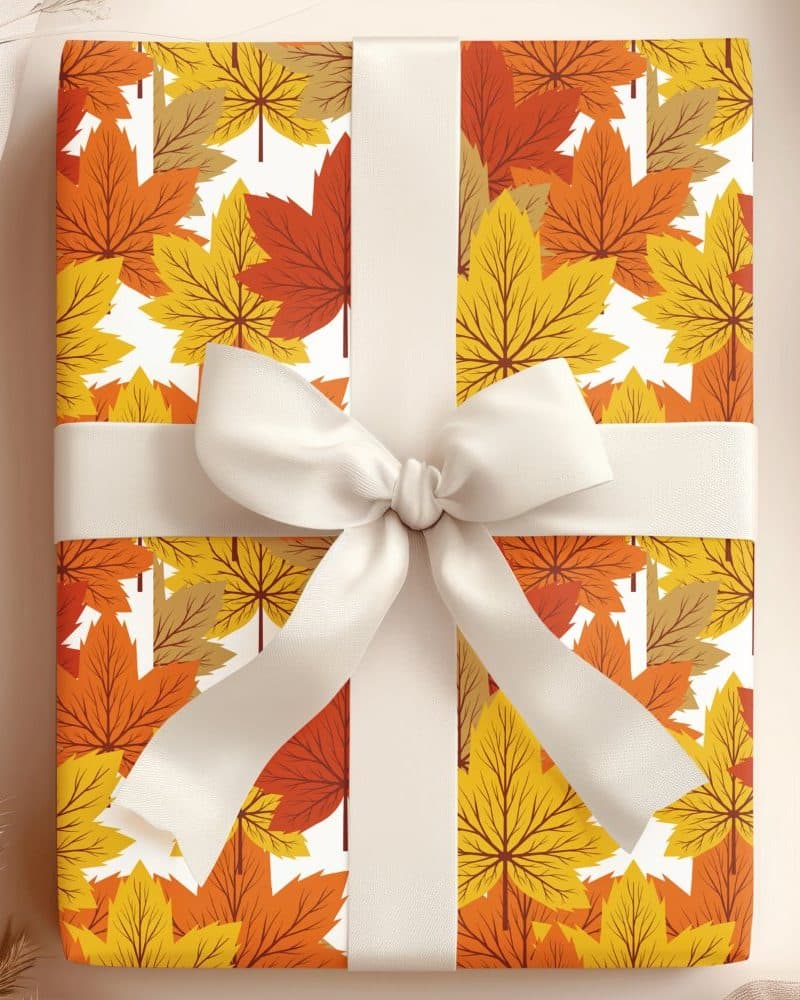 A gift wrapped in autumn-themed wrapping paper featuring orange and yellow leaves, tied with a cream-colored ribbon.