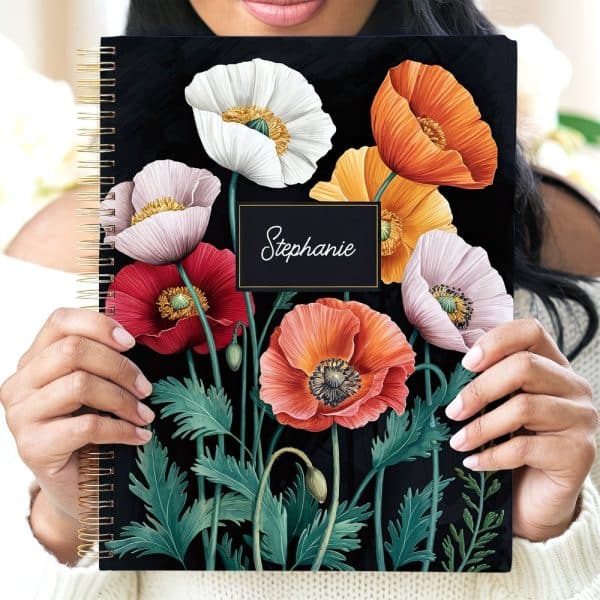 Person Holding A Spiral-Bound Notebook With A Dark Background Featuring A Bouquet Of Colorful Poppies And The Name Stephanie.