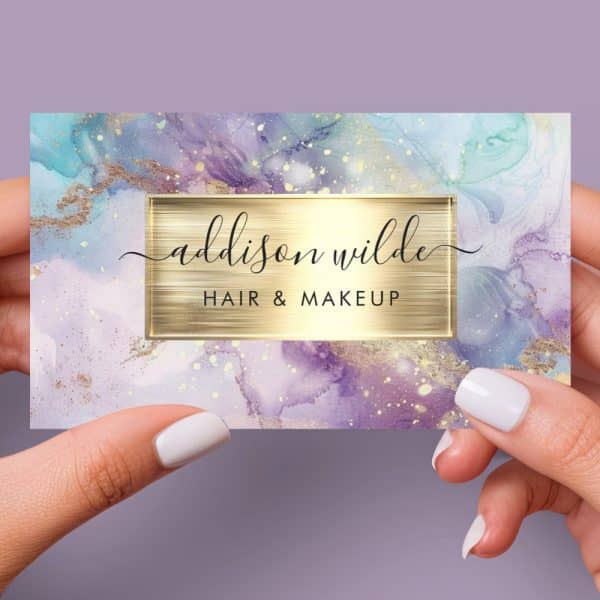 A Business Card For Addison Wilde Hair &Amp; Makeup, Featuring A Purple And Teal Watercolor Design With Gold Accents.