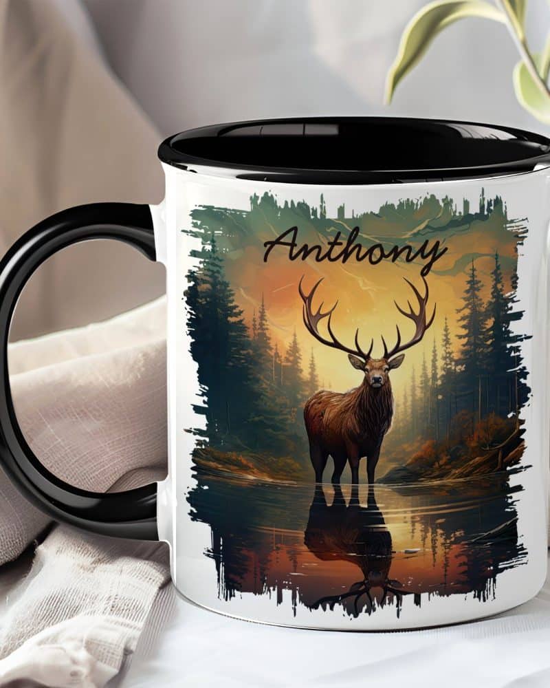 A black and white mug with a black handle, featuring a large stag standing in a forest reflecting in water at sunset. The name Anthony is printed on the mug.