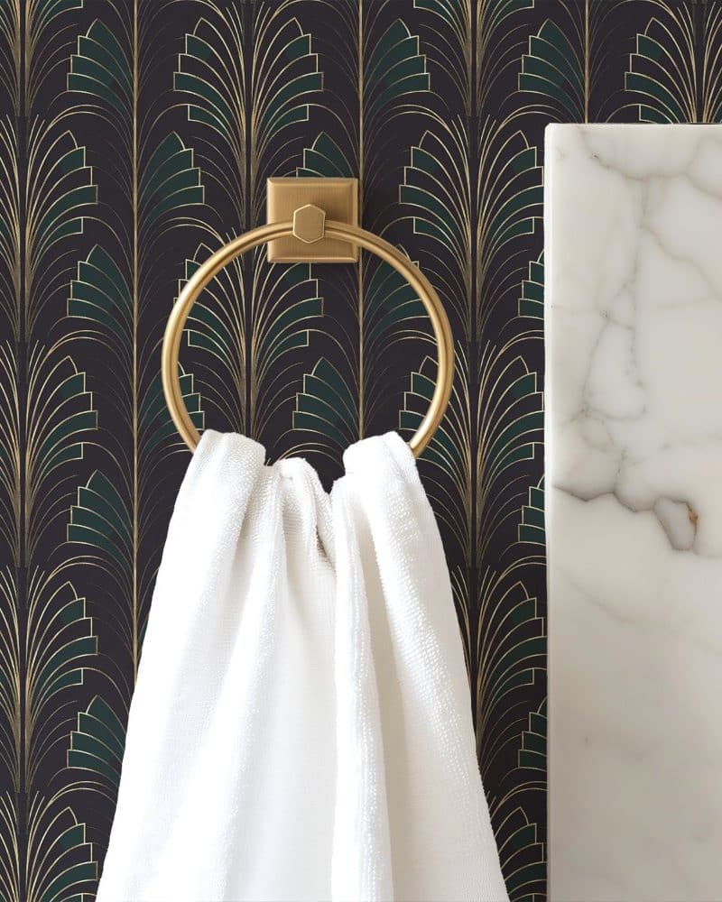 White towel hanging on a gold ring against a dark Art Deco wallpaper.