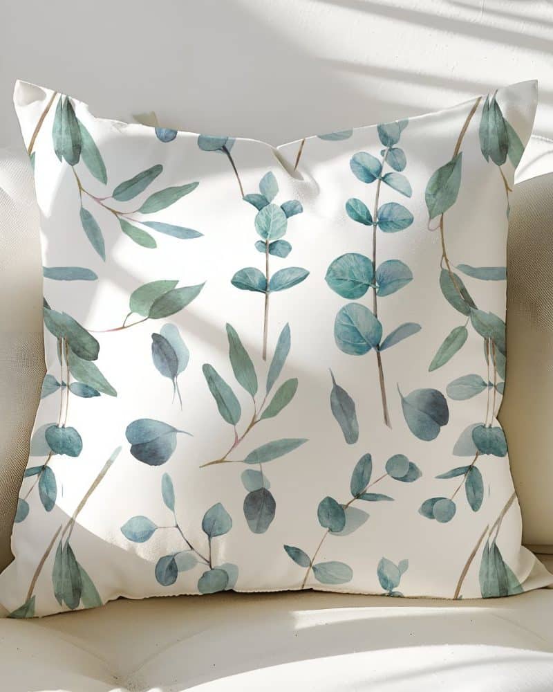 White throw pillow with a repeating pattern of light blue-green eucalyptus leaves.