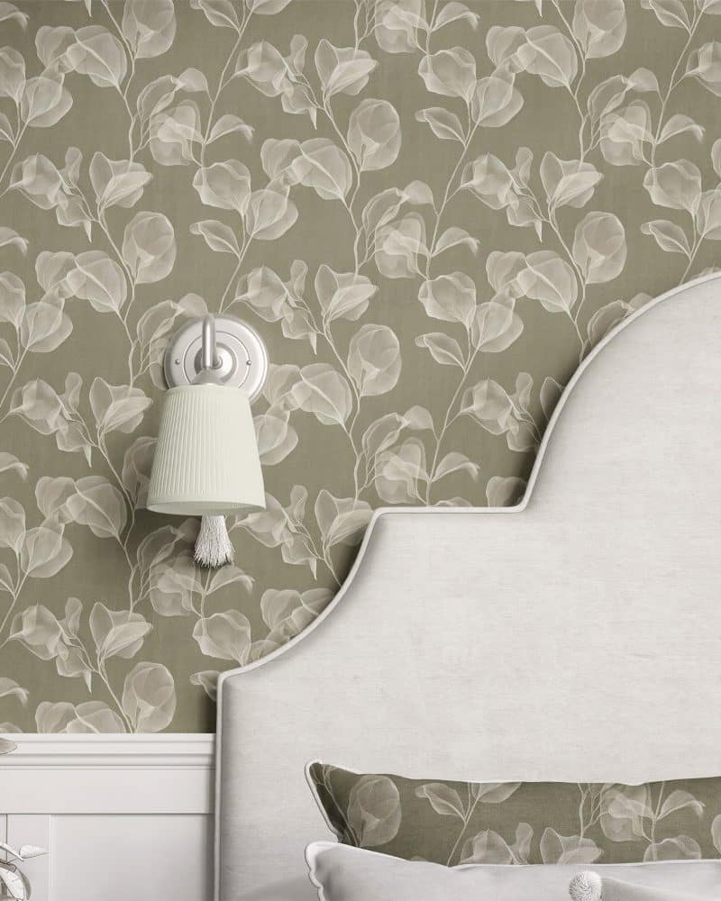 A curved headboard with a matching pillow sits against a wall covered in olive green wallpaper featuring a pattern of translucent white leaves.