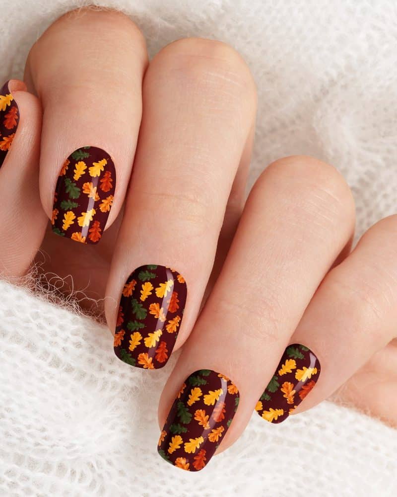 Close-up of fingernails with autumn leaf nail art.