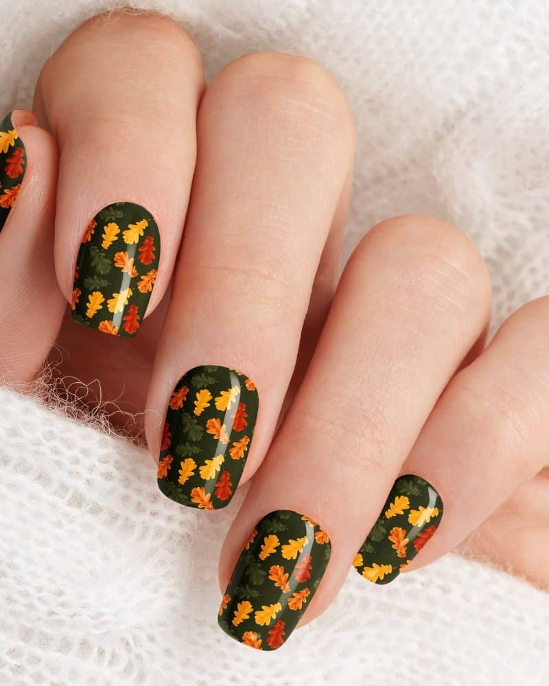 Autumn leaf nail art on a hand resting on a white sweater.