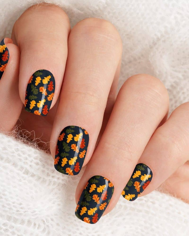 Close-up of a hand with nails decorated with autumn leaf designs.