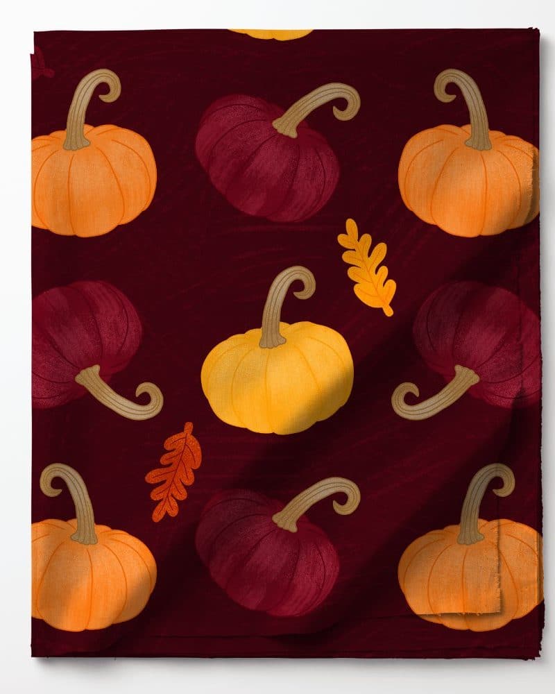 Burgundy fabric with a repeating pattern of orange, yellow, and maroon pumpkins and autumn leaves.