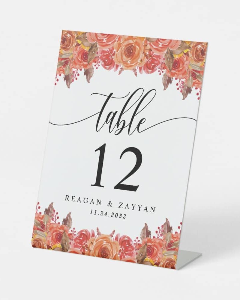Wedding table number twelve, with peach and orange floral accents, and the names Reagan & Zayyan and date 11.24.2033.