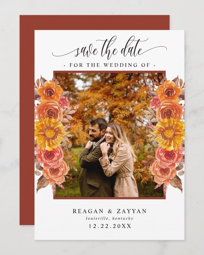Save the date card with a photo of a couple embracing, framed by autumnal flowers.