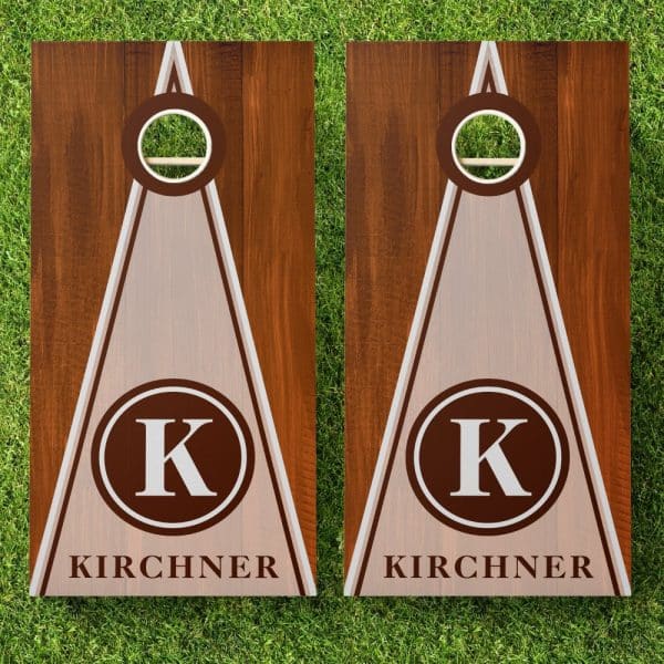 Pair Of Personalized Cornhole Boards With A Brown Wood Grain Finish, Off-White Triangle Design, And The Initial K In A Brown Circle, Along With The Last Name Kirchner.