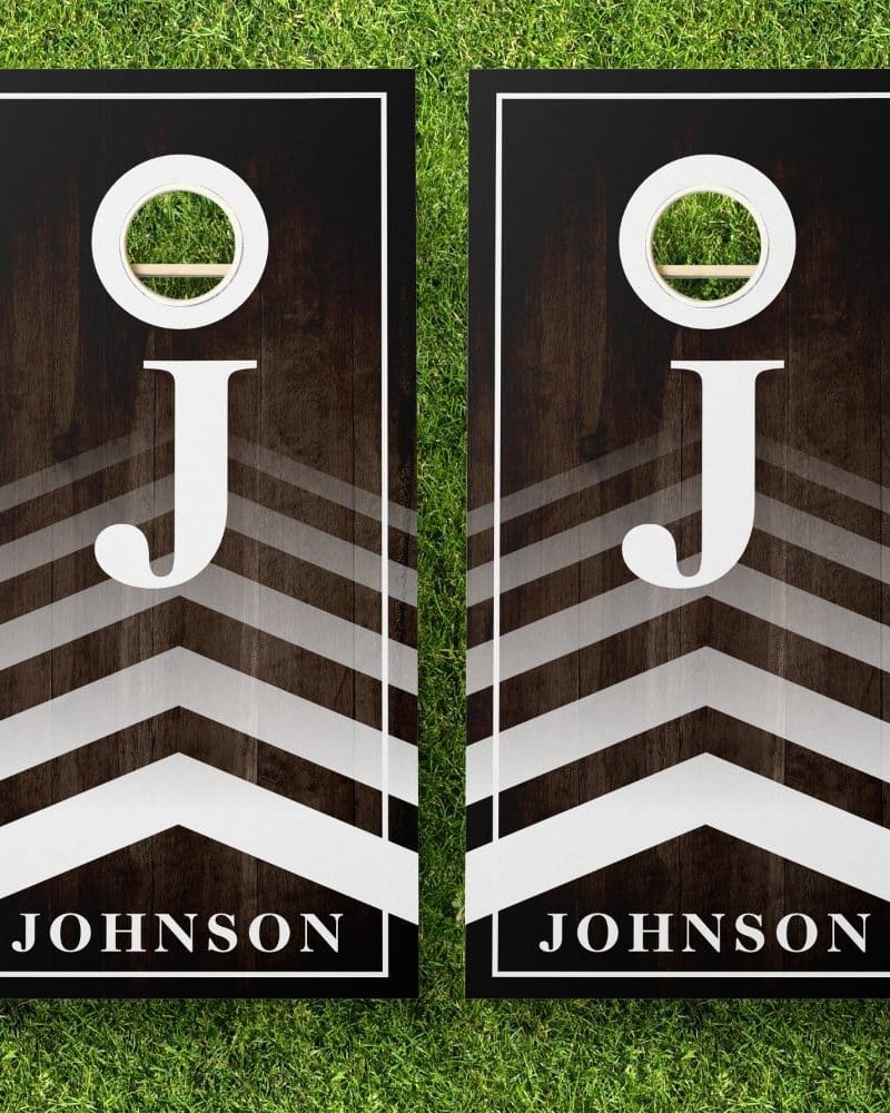 Pair of personalized cornhole boards with a dark wood grain background, chevron pattern, and large white J initial, along with the name Johnson.