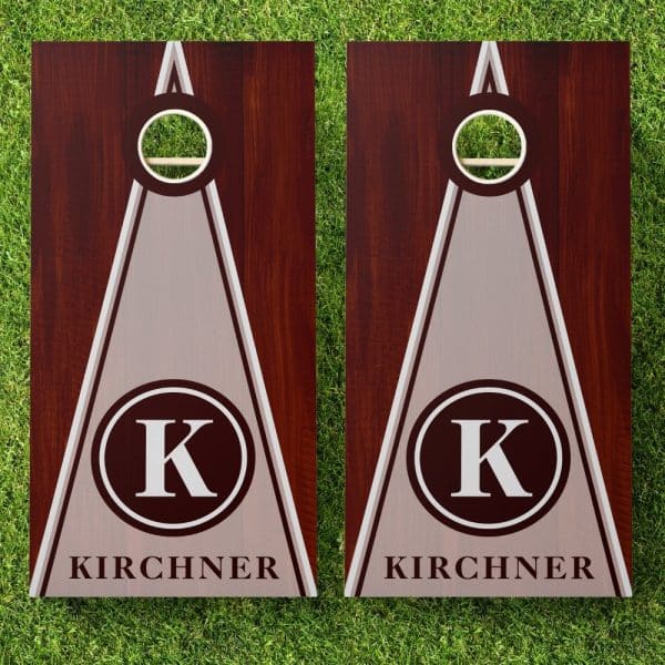Pair Of Personalized Cornhole Boards With A Dark Wood Frame, Light Gray Triangle Center, And A Monogrammed K In A Dark Circle. The Name Kirchner Is Below The Monogram.