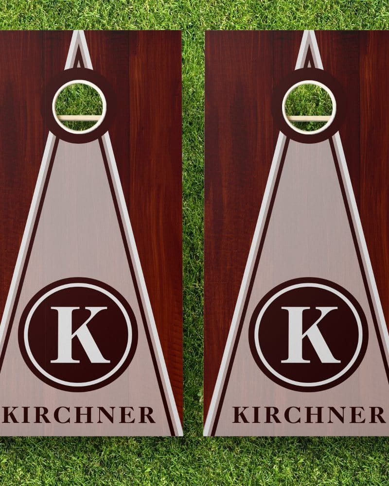 Pair of personalized cornhole boards with a dark wood frame, light gray triangle center, and a monogrammed K in a dark circle. The name Kirchner is below the monogram.