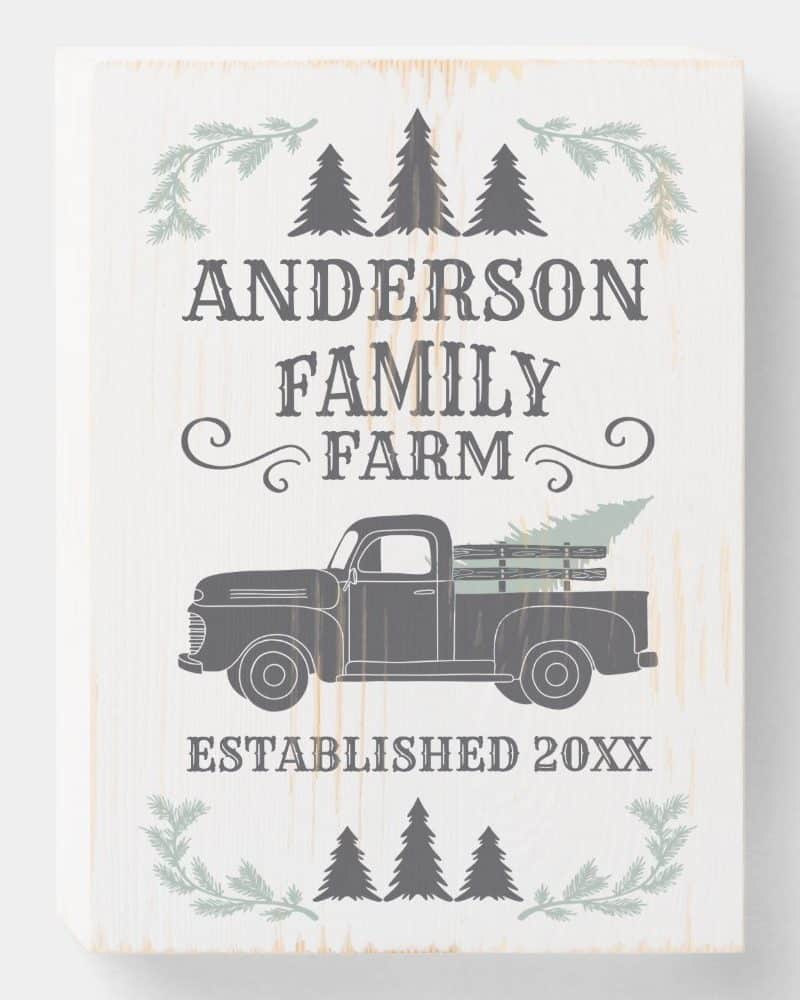 White wooden sign with the Anderson Family Farm logo, featuring a vintage truck carrying a Christmas tree.