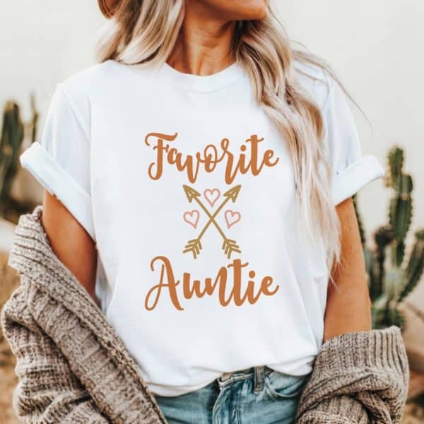 White T-Shirt With The Text Favorite Auntie In Orange Lettering, Accented With A Design Of Crossed Arrows And Hearts.