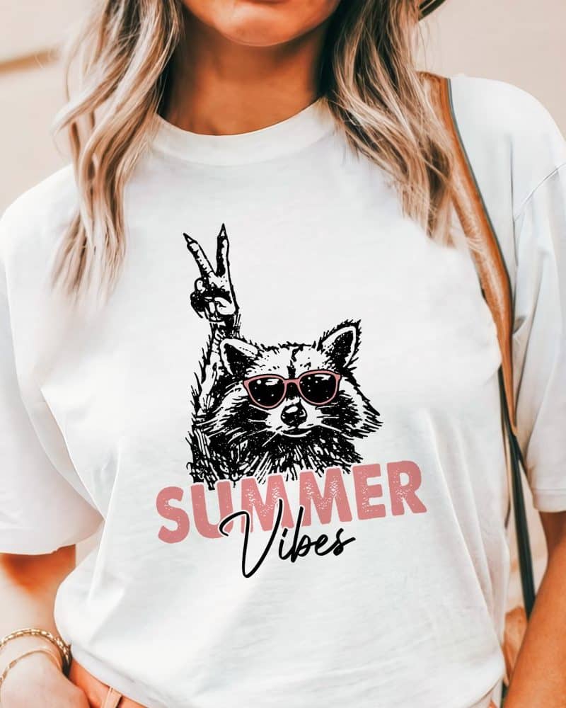 White t-shirt featuring a graphic of a raccoon wearing sunglasses and giving a peace sign, with the text Summer Vibes.