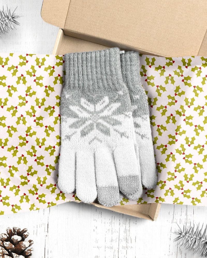 Grey and white knit gloves with a snowflake pattern, presented in a gift box lined with holly-patterned paper.