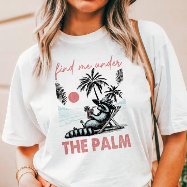 White T-Shirt Featuring A Raccoon Lounging In A Beach Chair Under Palm Trees, Holding A Drink. Text Reads Find Me Under The Palm.
