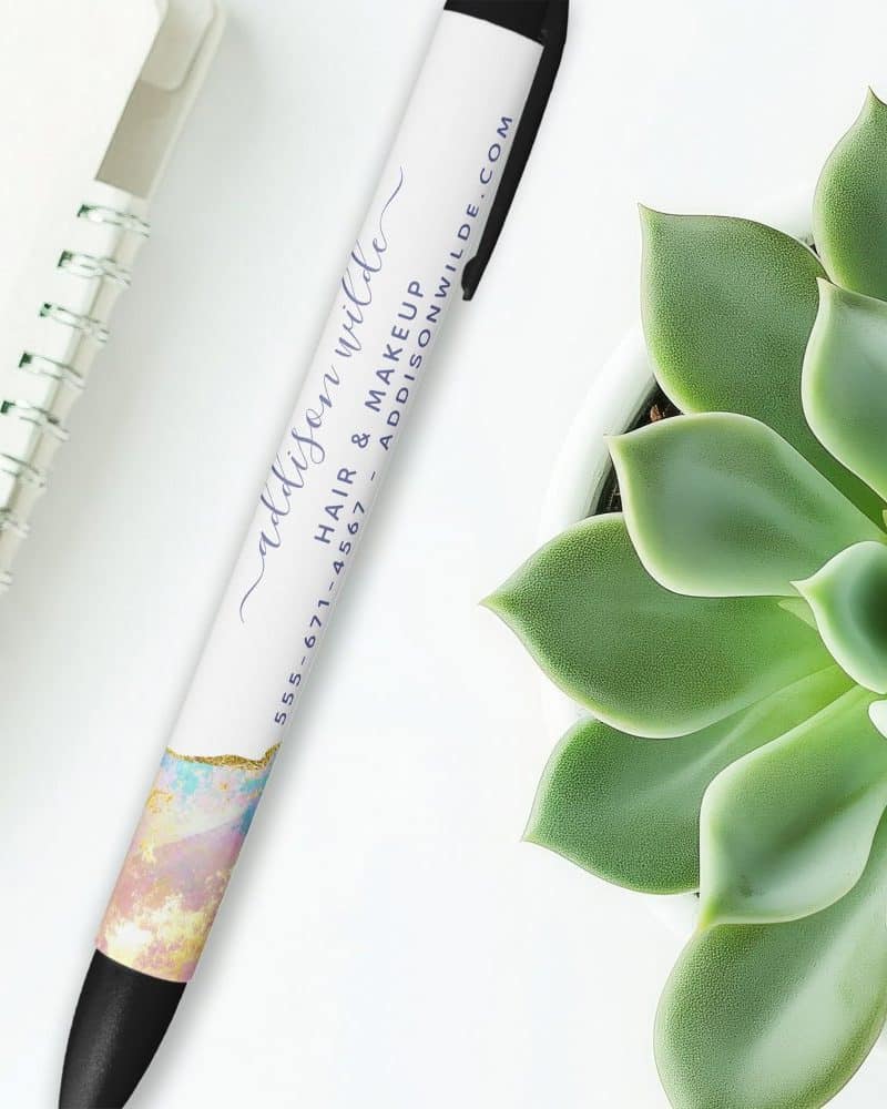 A pen with a pastel marble design and Addison Wilde's hair and makeup business information printed on it.