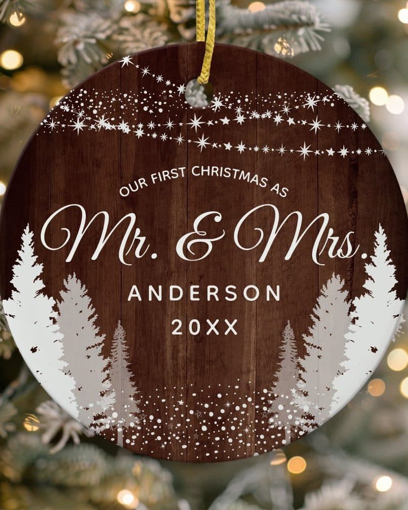 Round Christmas ornament with a wood grain background, featuring a snowy winter scene with trees and the text "Our First Christmas as Mr. & Mrs. Anderson 20XX".