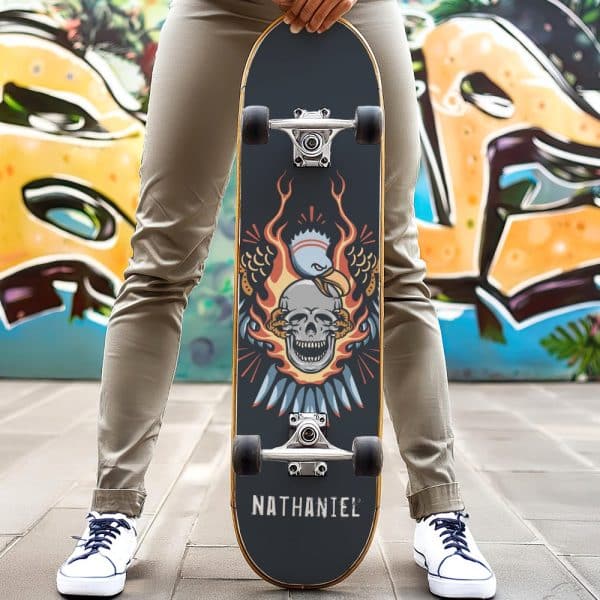 Person Holding A Skateboard With A Skull Engulfed In Flames And Eagle Wings Design. The Name Nathaniel Is On The Bottom.