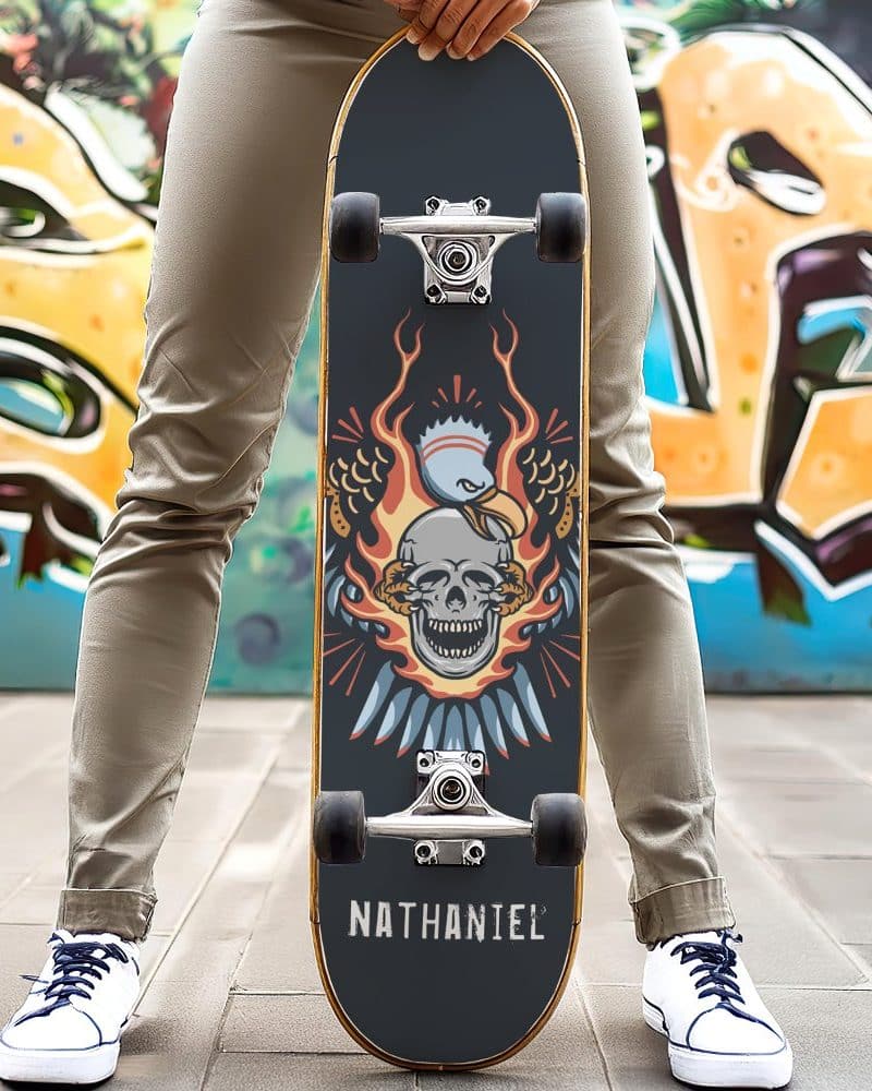 Person holding a skateboard with a skull engulfed in flames and eagle wings design. The name Nathaniel is on the bottom.