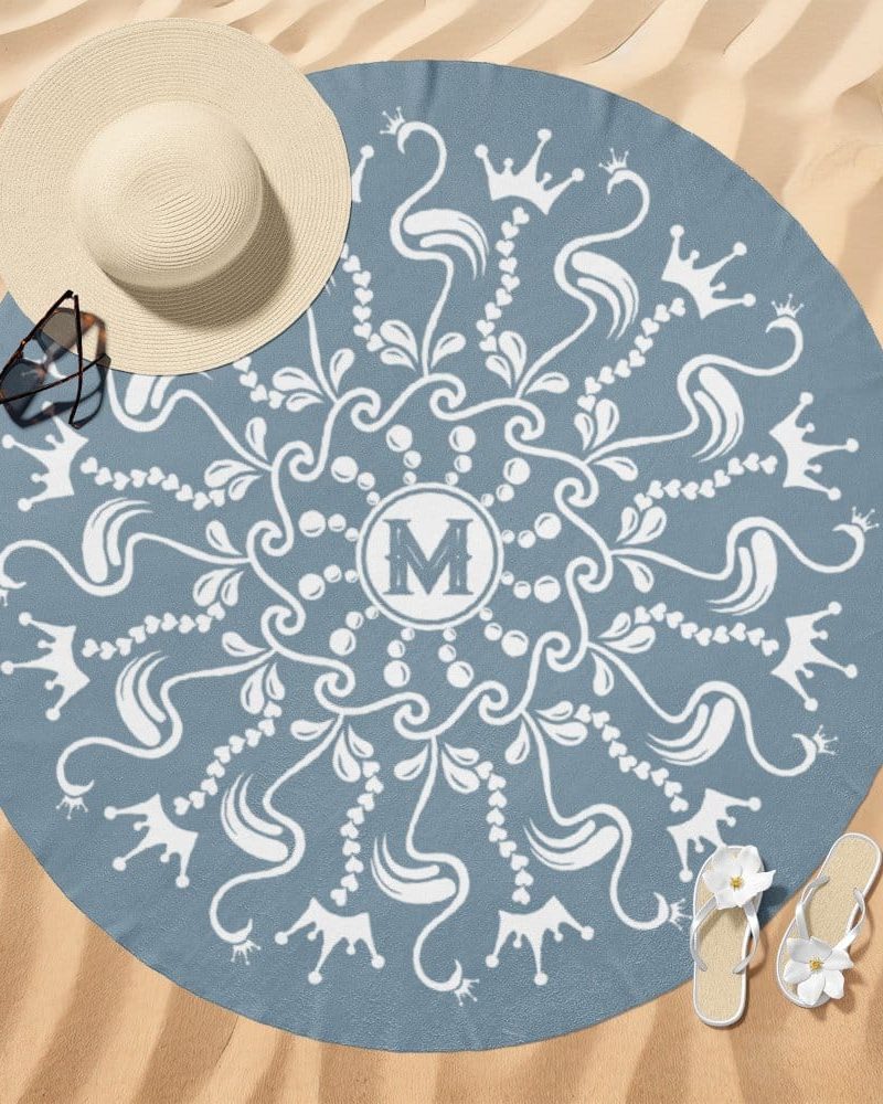 Blue round beach towel with a white mandala design, featuring crowns and the letter M in the center.