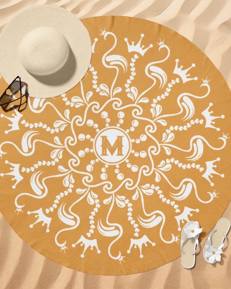 Mustard yellow round beach towel with a white mandala design featuring crowns and the letter M in the center.