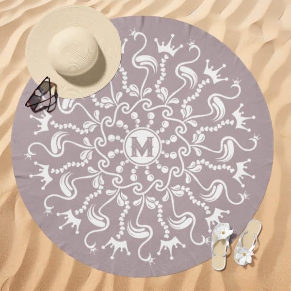 A Mauve Round Beach Towel With A White Mandala Design Featuring Crowns And The Letter M In The Center.