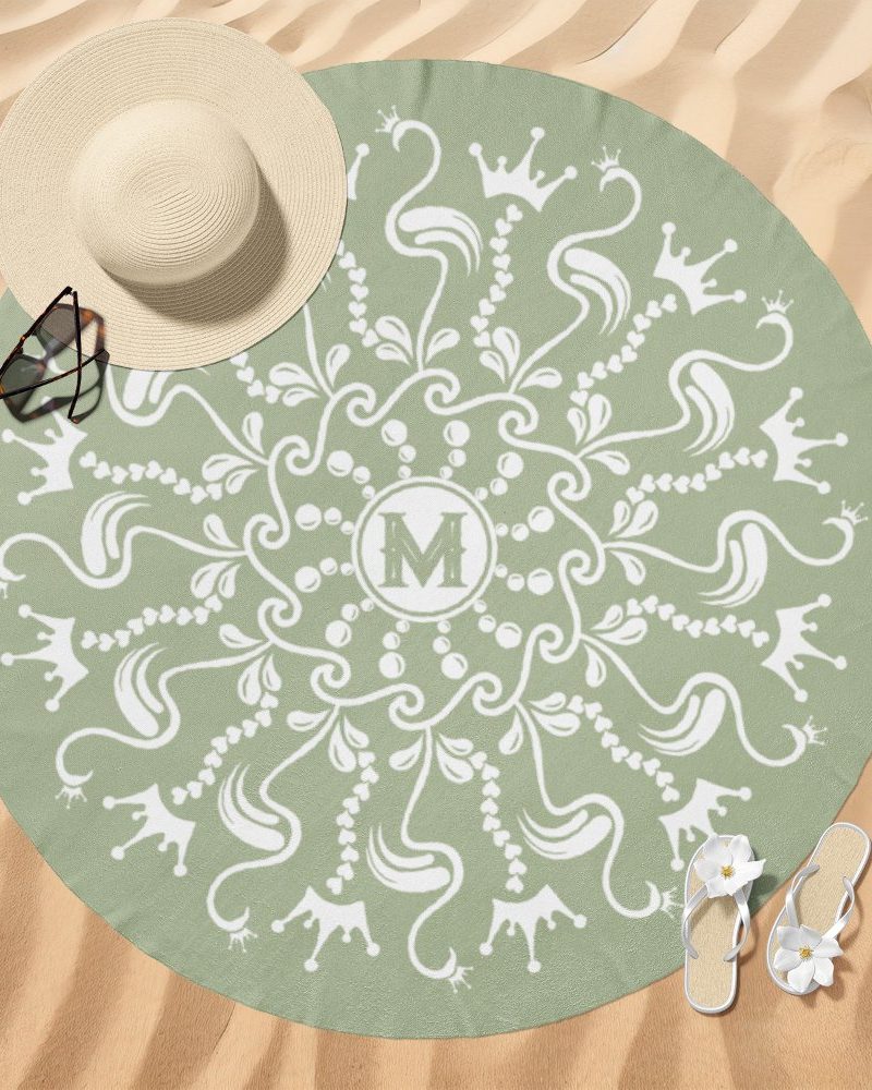 Sage green round beach towel with a white mandala design featuring crowns and an initial M in the center.