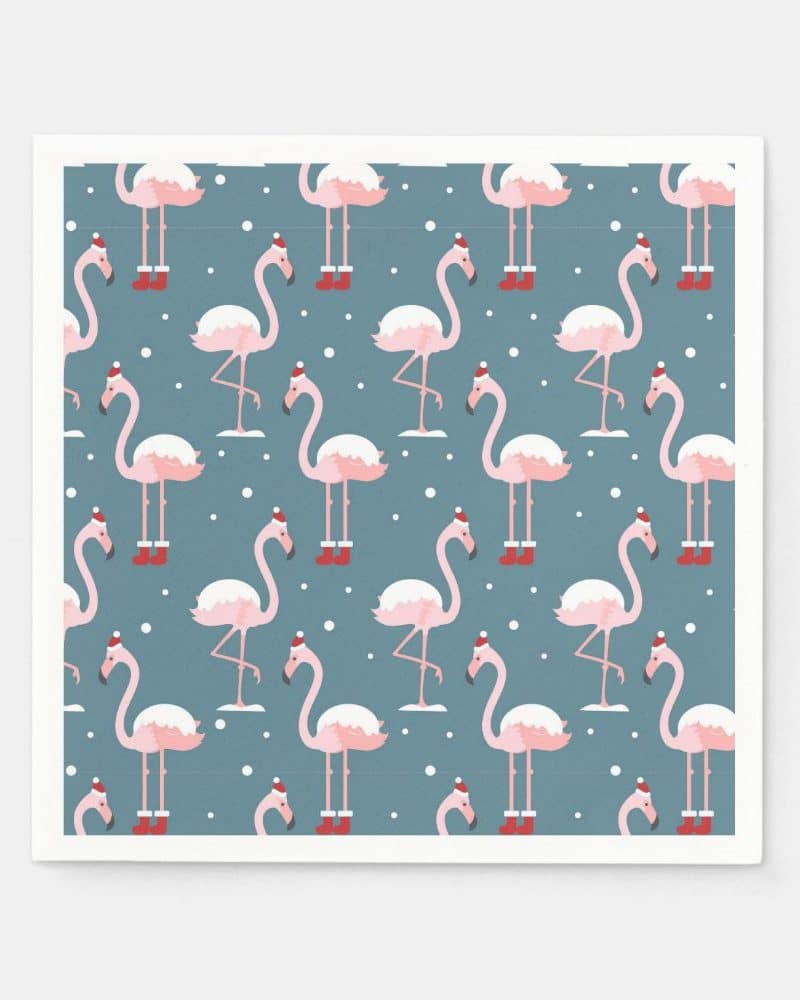 A repeating pattern of pink flamingos wearing Santa hats and boots on a blue background with white snowflakes.