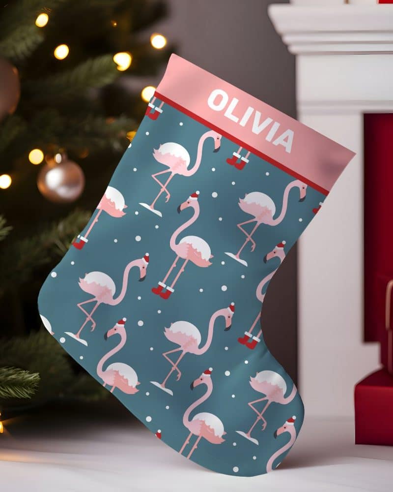 Personalized Christmas stocking with a teal background and a repeating pattern of pink flamingos wearing Santa hats. The stocking is labeled Olivia.