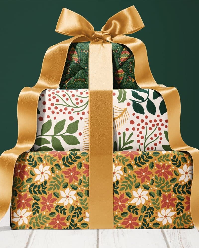 Stack of three Christmas presents wrapped in festive patterned paper and tied with a large gold ribbon.
