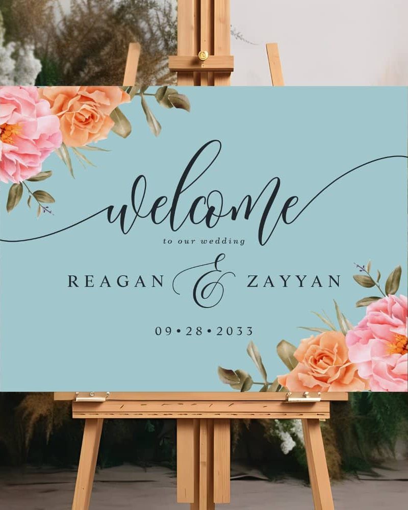 Light blue wedding welcome sign with floral corners and the names Reagan and Zayyan, and the date September 28, 2033.