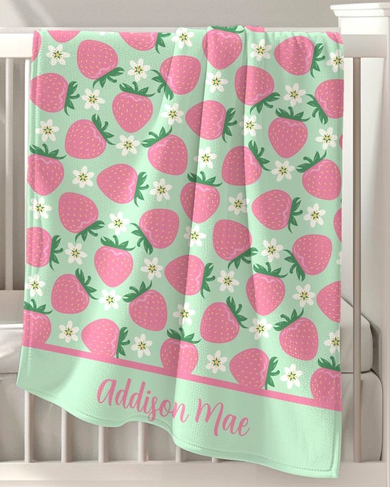 Mint green baby blanket with a pink strawberry and flower pattern and personalized name.