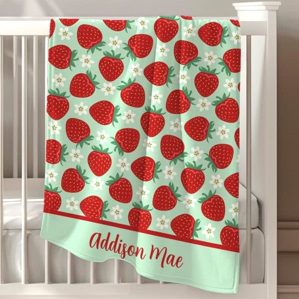 A Light Green Baby Blanket With A Repeating Pattern Of Red Strawberries And White Flowers, Personalized With The Name Addison Mae.