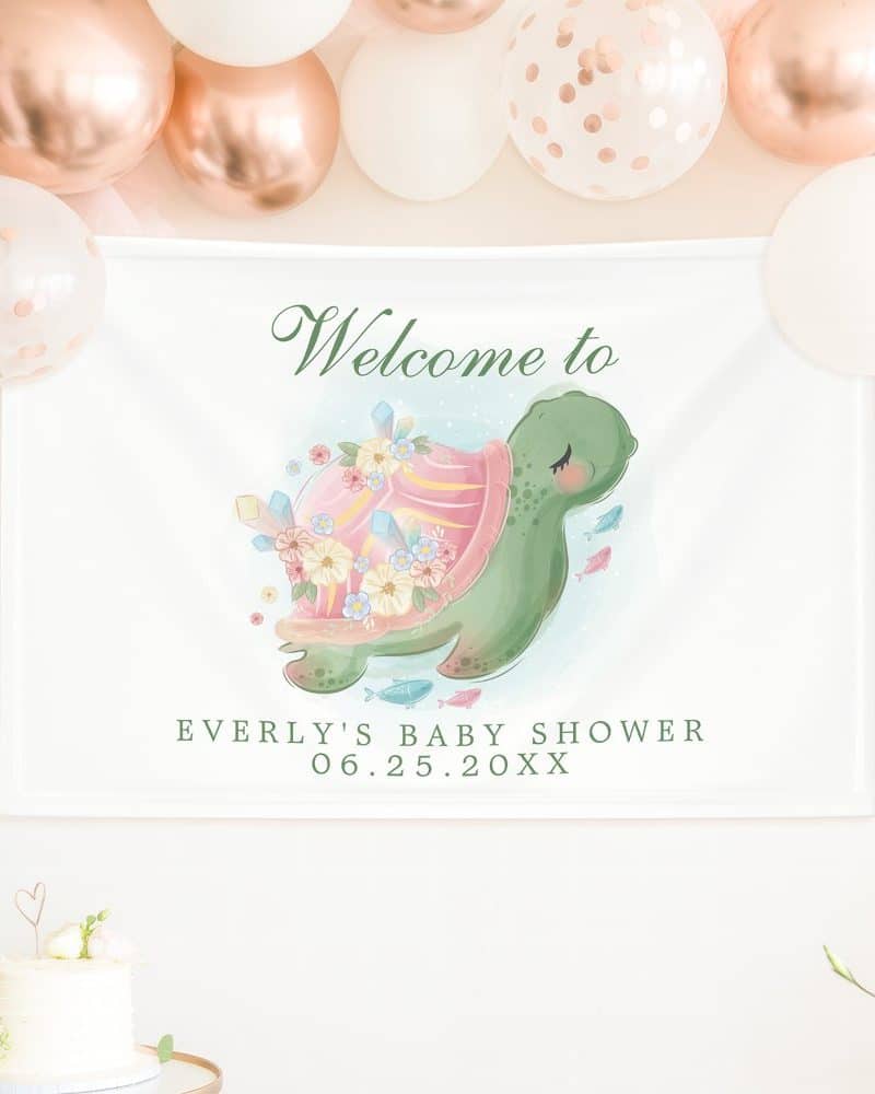 Baby shower banner featuring a whimsical illustration of a turtle adorned with flowers and crystals. The banner also includes the baby's name and shower date.