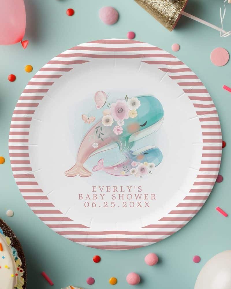Pink and white striped paper plate with watercolor illustration of two whales adorned with flowers, butterflies, and the text Everly's Baby Shower and date.