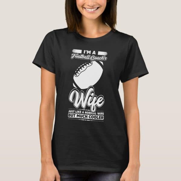 Woman Wearing A Black T-Shirt That Says Im A Football Coachs Wife, With A Football Graphic And The Phrase Just Like A Normal Wife But Much Cooler.