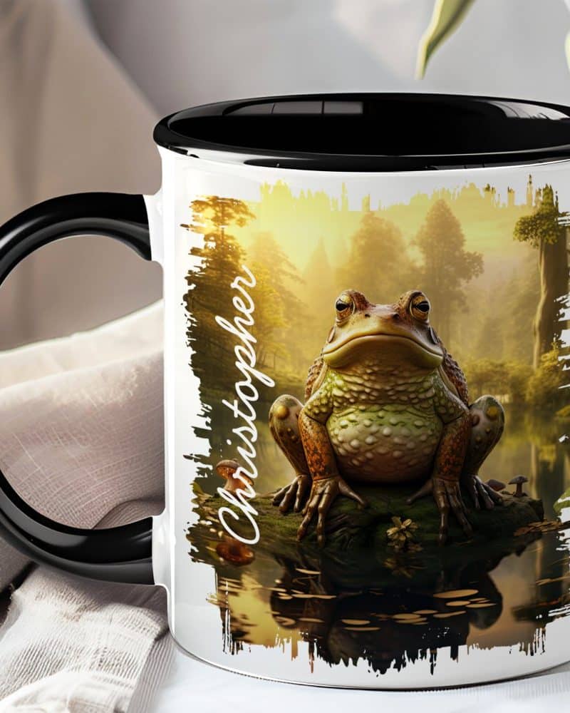 White coffee mug with a black handle and rim, featuring a large toad sitting by water in a forest scene. The name Christopher is printed on the mug.