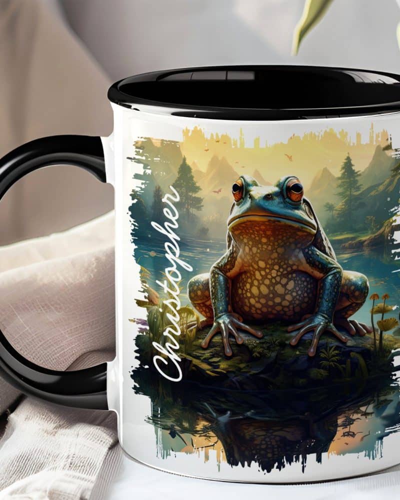 Black-handled mug with a colorful illustration of a large frog sitting on a rock by a lake, the name Christopher is written on the side.