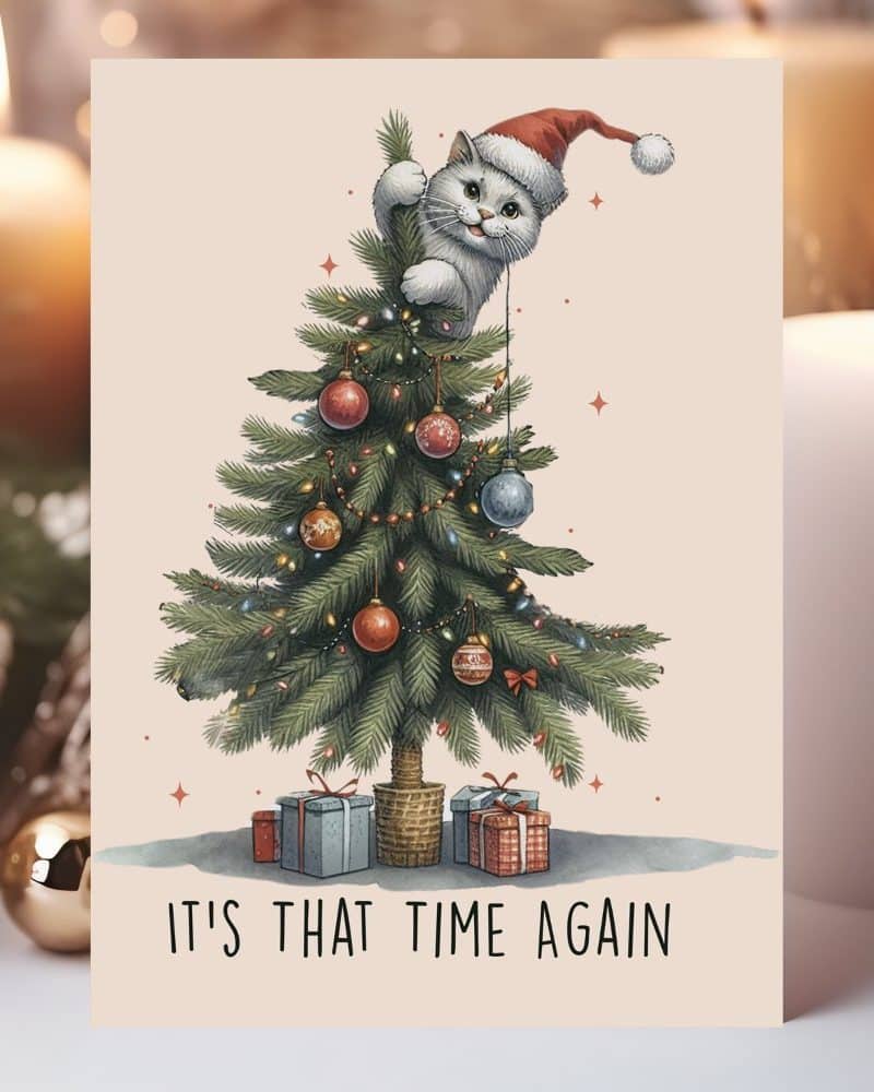 Christmas card featuring a white cat wearing a Santa hat perched on a decorated Christmas tree. The text "It's that time again" is below.
