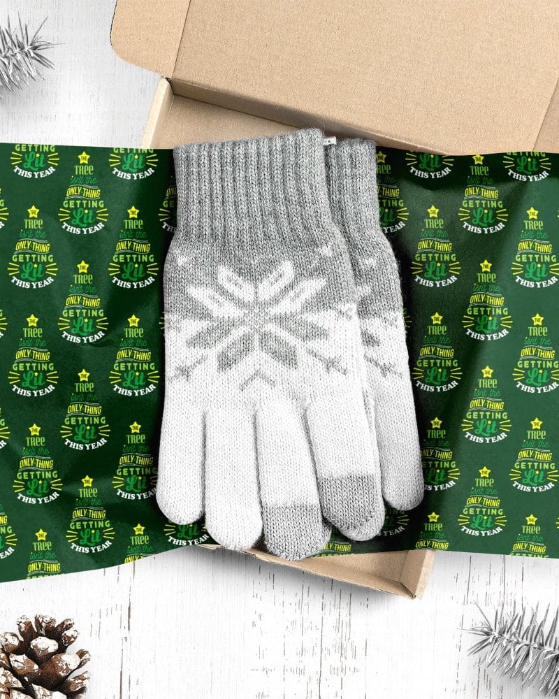Gray knit gloves with a snowflake pattern, presented in a gift box lined with green Christmas wrapping paper.