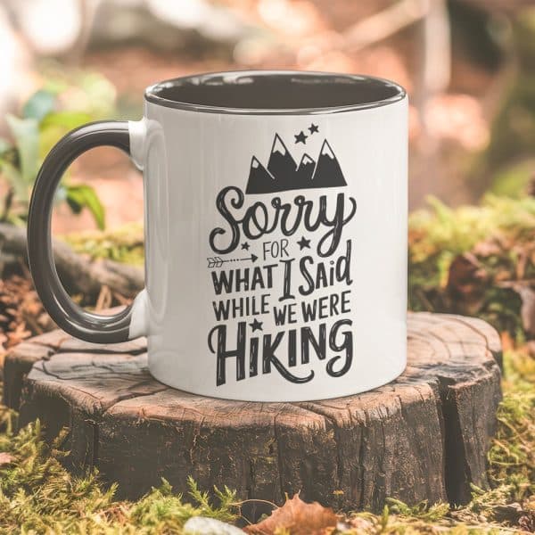 White Coffee Mug With Black Lettering That Says Sorry For What I Said While We Were Hiking, And A Graphic Of Mountains.