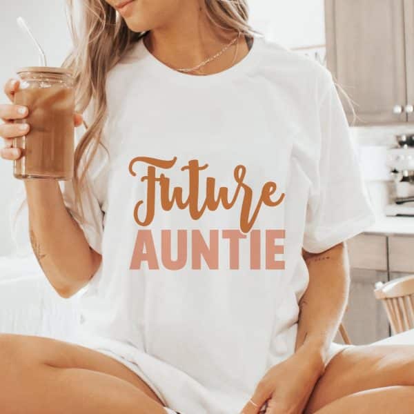 Woman Wearing A White T-Shirt That Says Future Auntie In A Tan And Peach Colored Script.